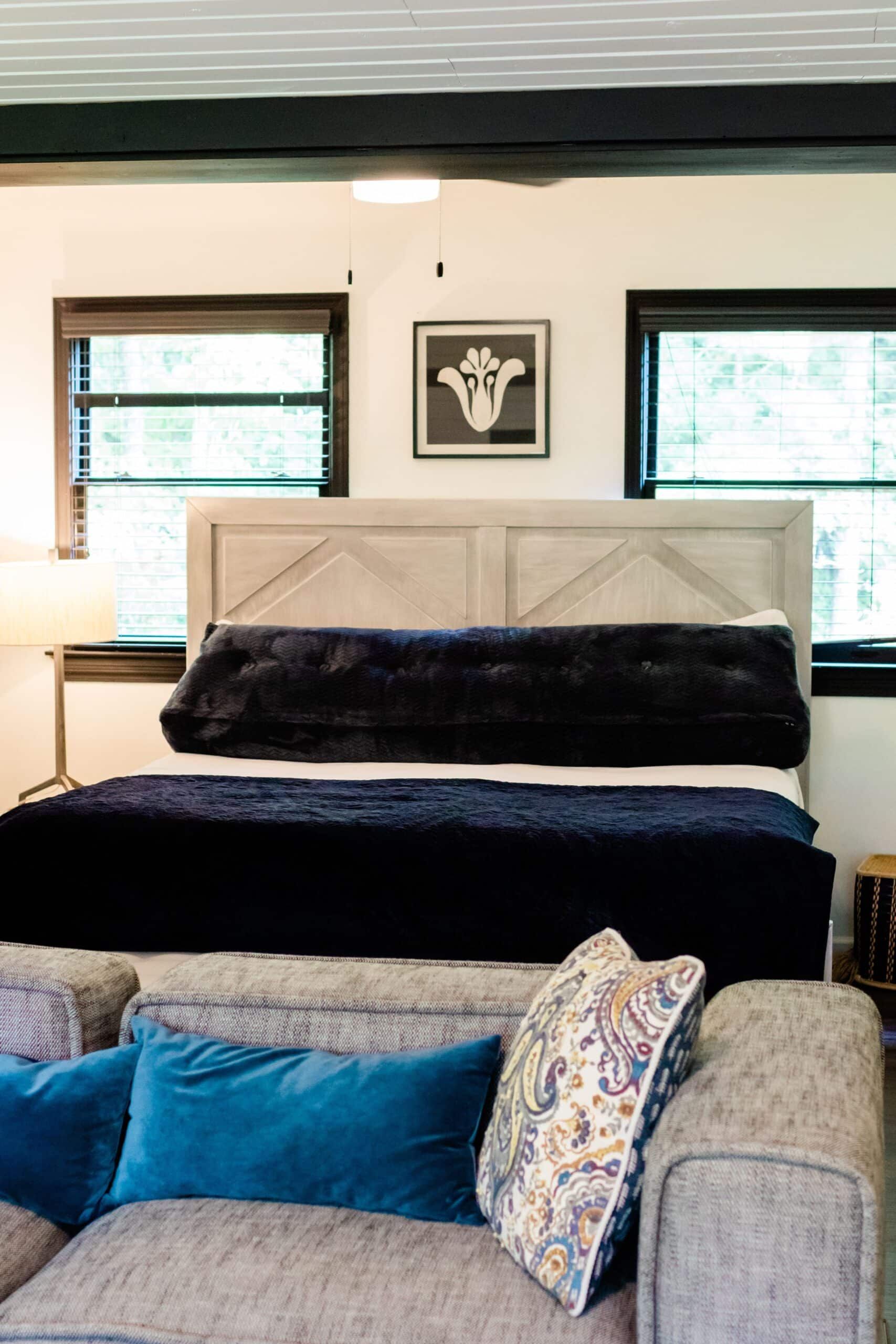 A bedroom with a bed , couch , and two windows.