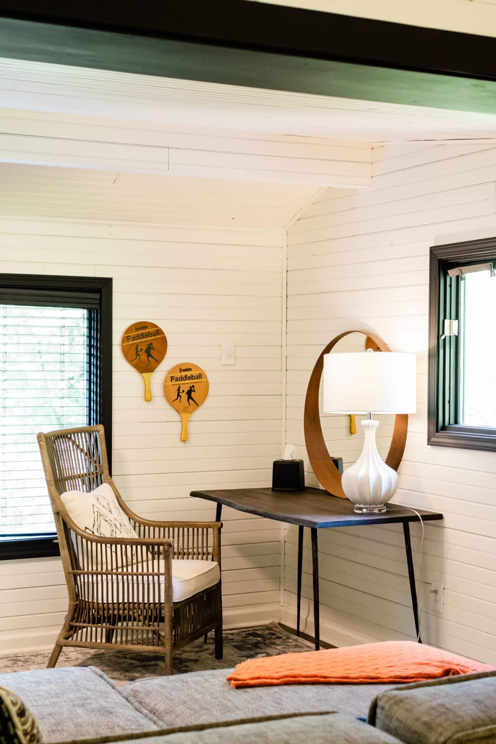 A living room with a table , chair , lamp and mirror.