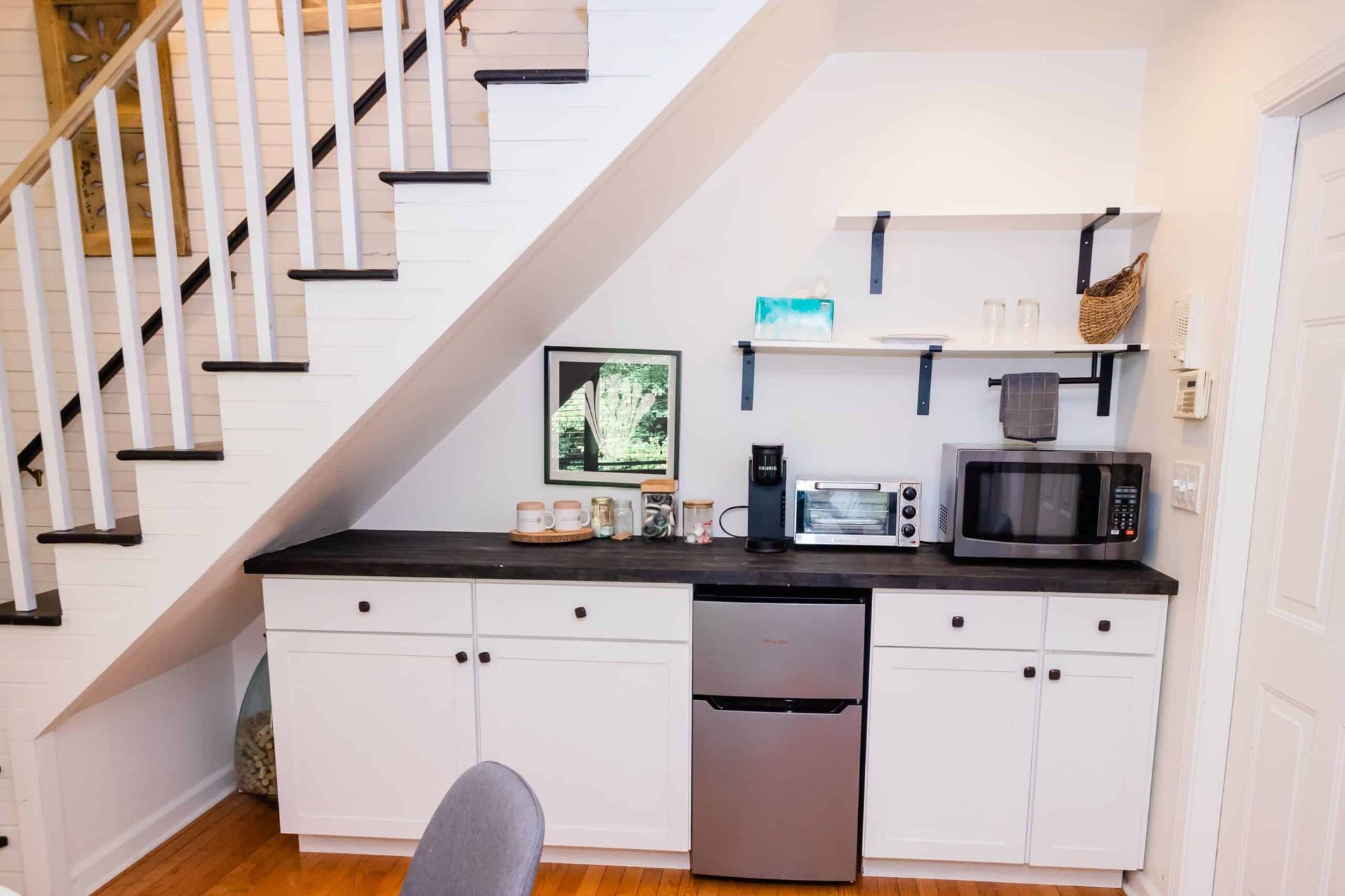 A kitchen with a refrigerator , microwave , and dishwasher under a staircase.