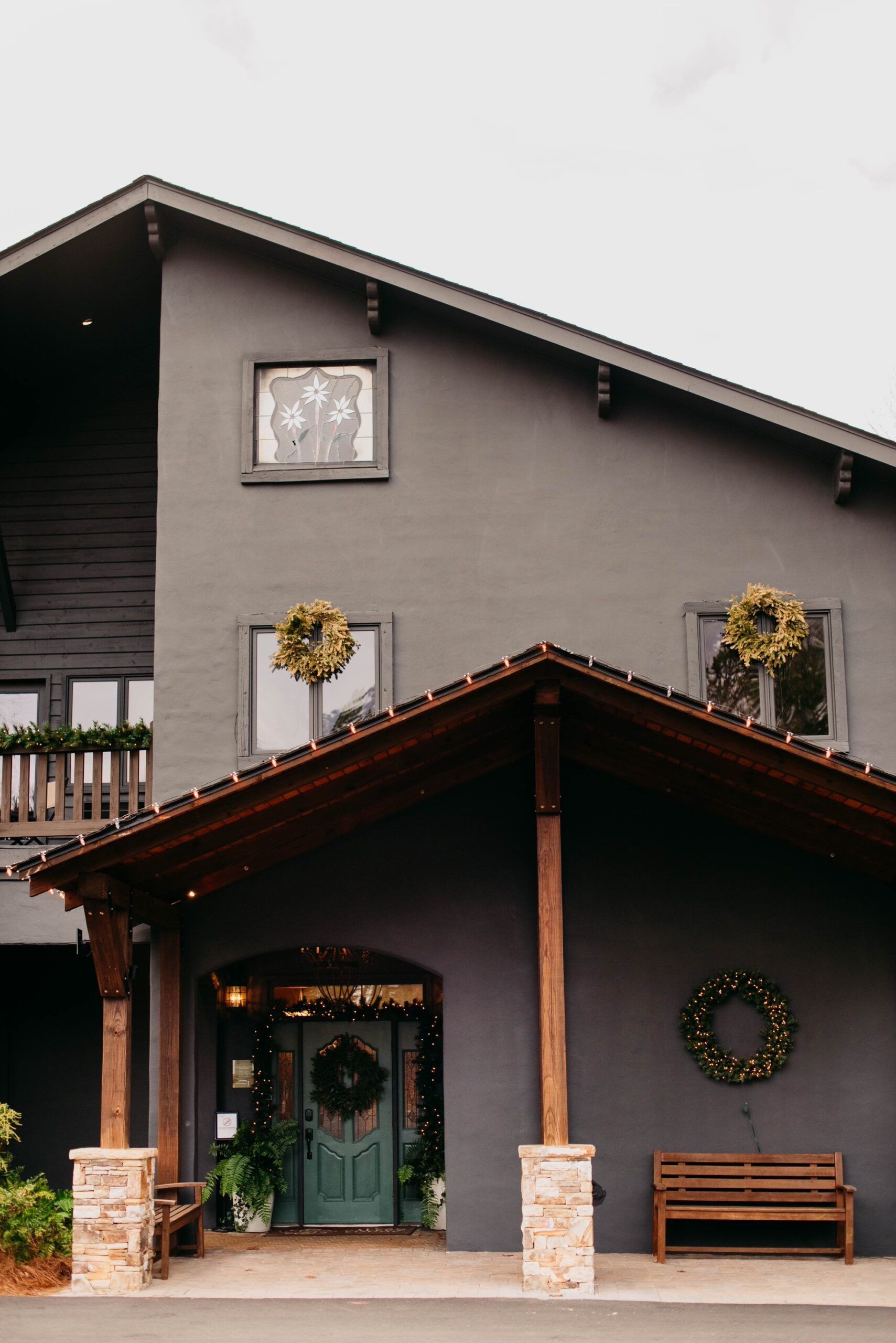 A large gray house with a porch and a bench in front of it.
