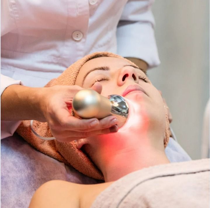 Mujer recibiendo un tratamiento facial con terapia de luz roja en un spa.