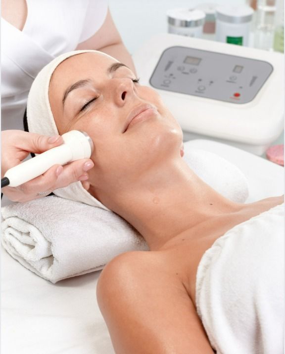 Mujer recibiendo un tratamiento facial, con un dispositivo aplicado en la mejilla, en un entorno de spa.