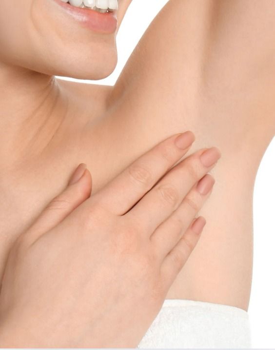 Persona tocándose la axila, mostrando piel suave y sin vello. Sonriendo, fondo blanco.