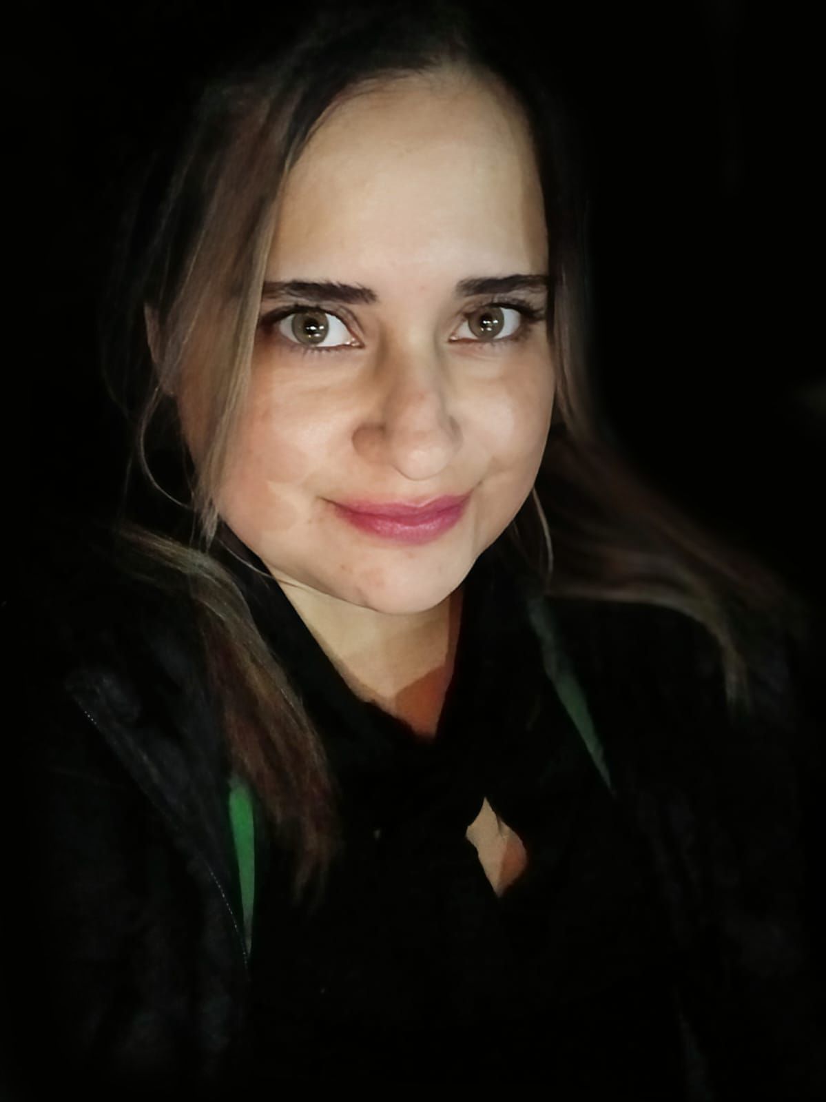 Mujer de ojos marrones y reflejos rubios, sonriendo. Vestida con ropa oscura, lleva pendientes de aro y tiene fondo oscuro.