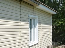 Beige vinyl-sided house exterior with a white-framed window and sloped roof
