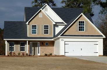 Suburban two-story beige house with a dark roof and white garage, front lawn under a cloudy sky
