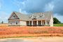 Newly built brick house with gray roof on a bare red dirt lot under a blue sky