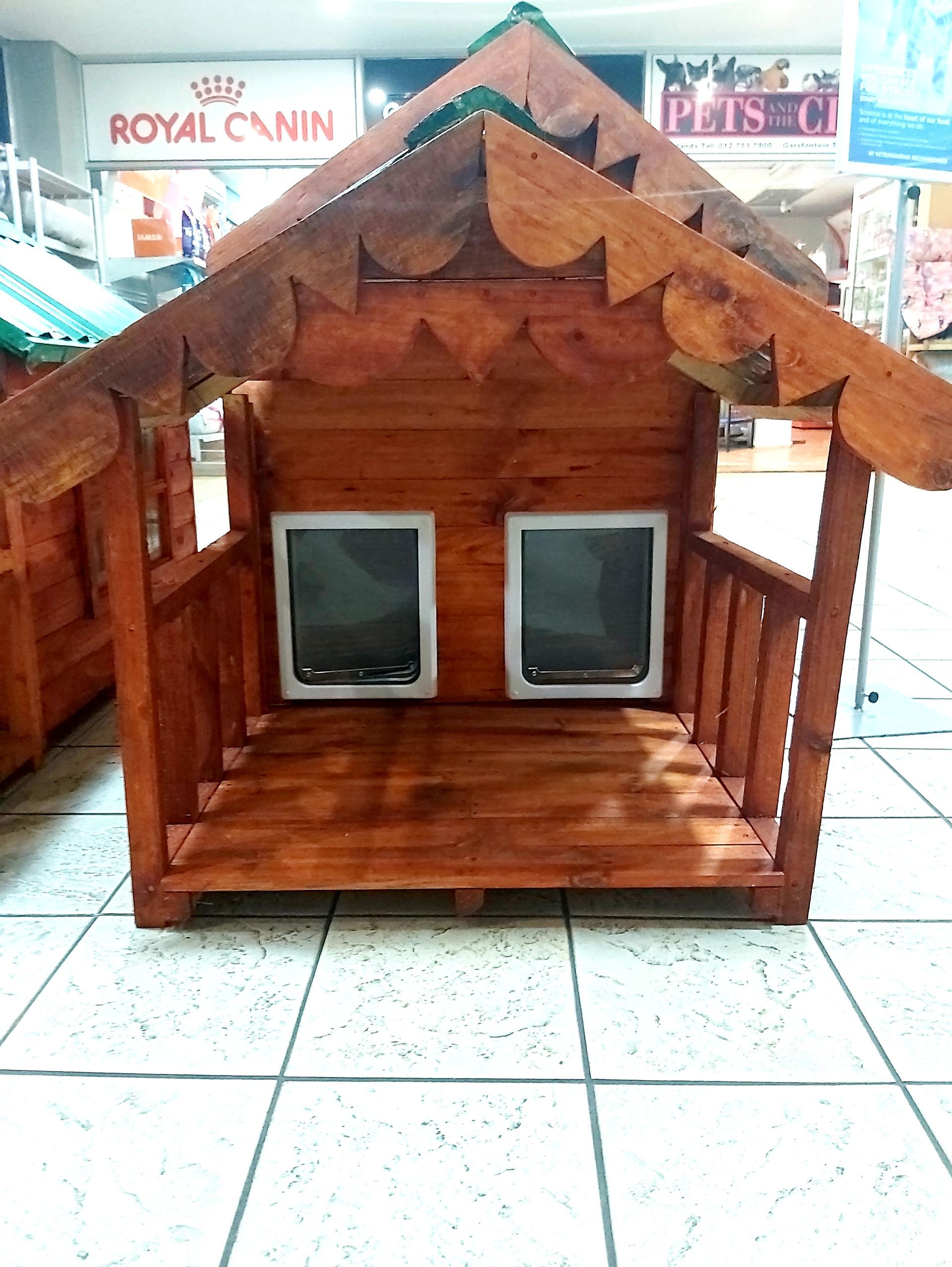 A wooden dog house is sitting on a tiled floor in front of a royal canin sign