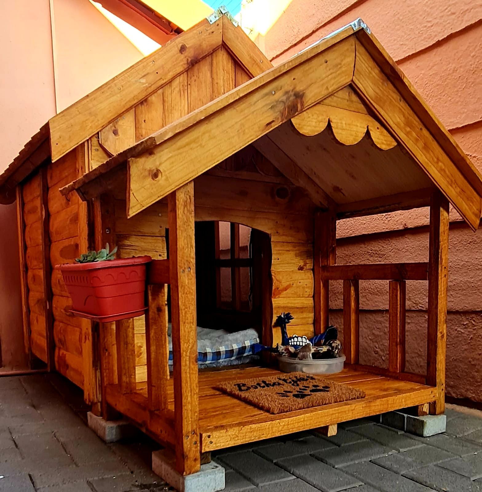 A wooden dog house with a welcome mat on the floor available at Pets and the City in Pretoria East.