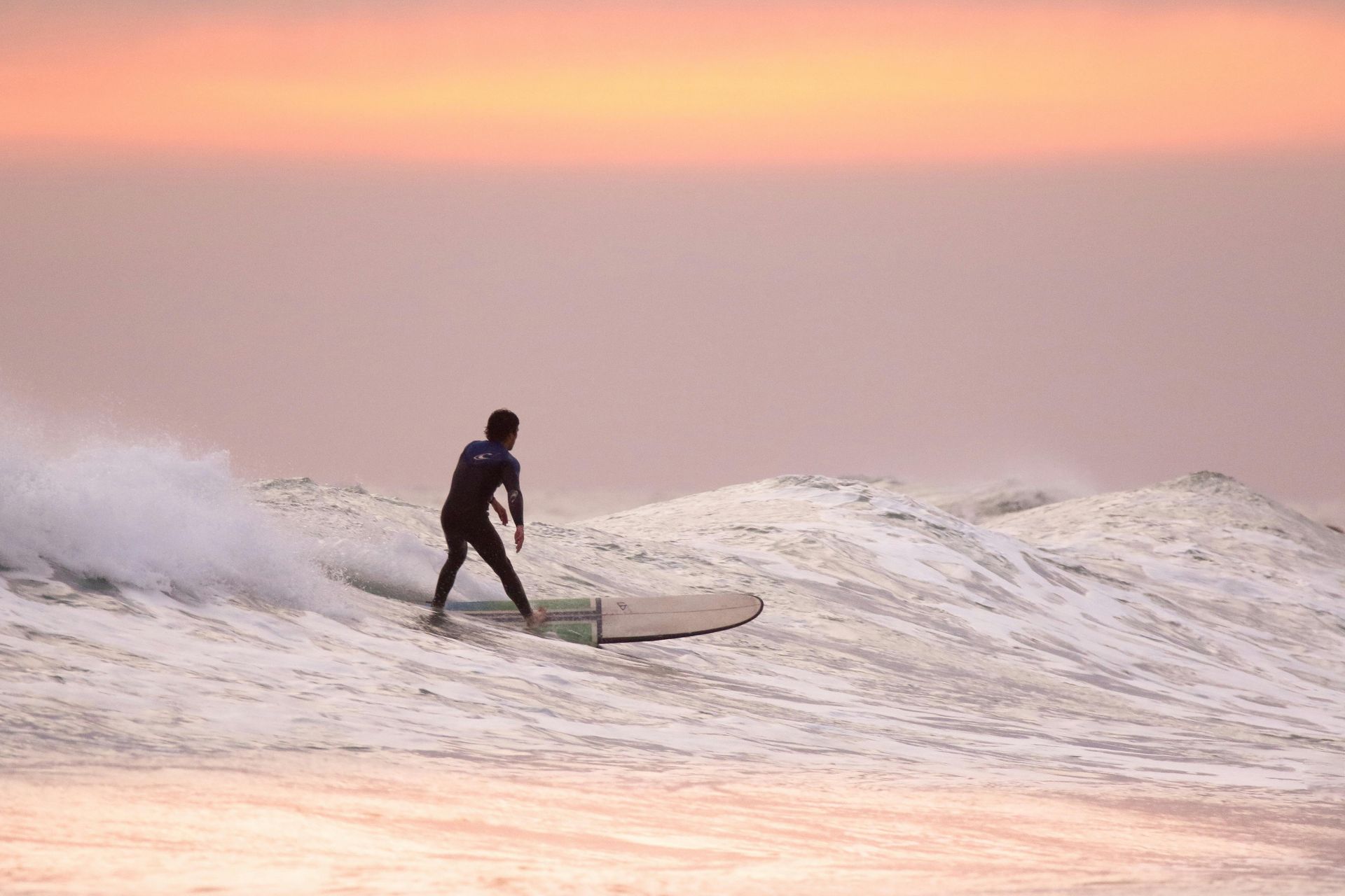 Cocoa Beach Surfer riding a wave at sunset, silhouette against pink and orange sky, ocean.