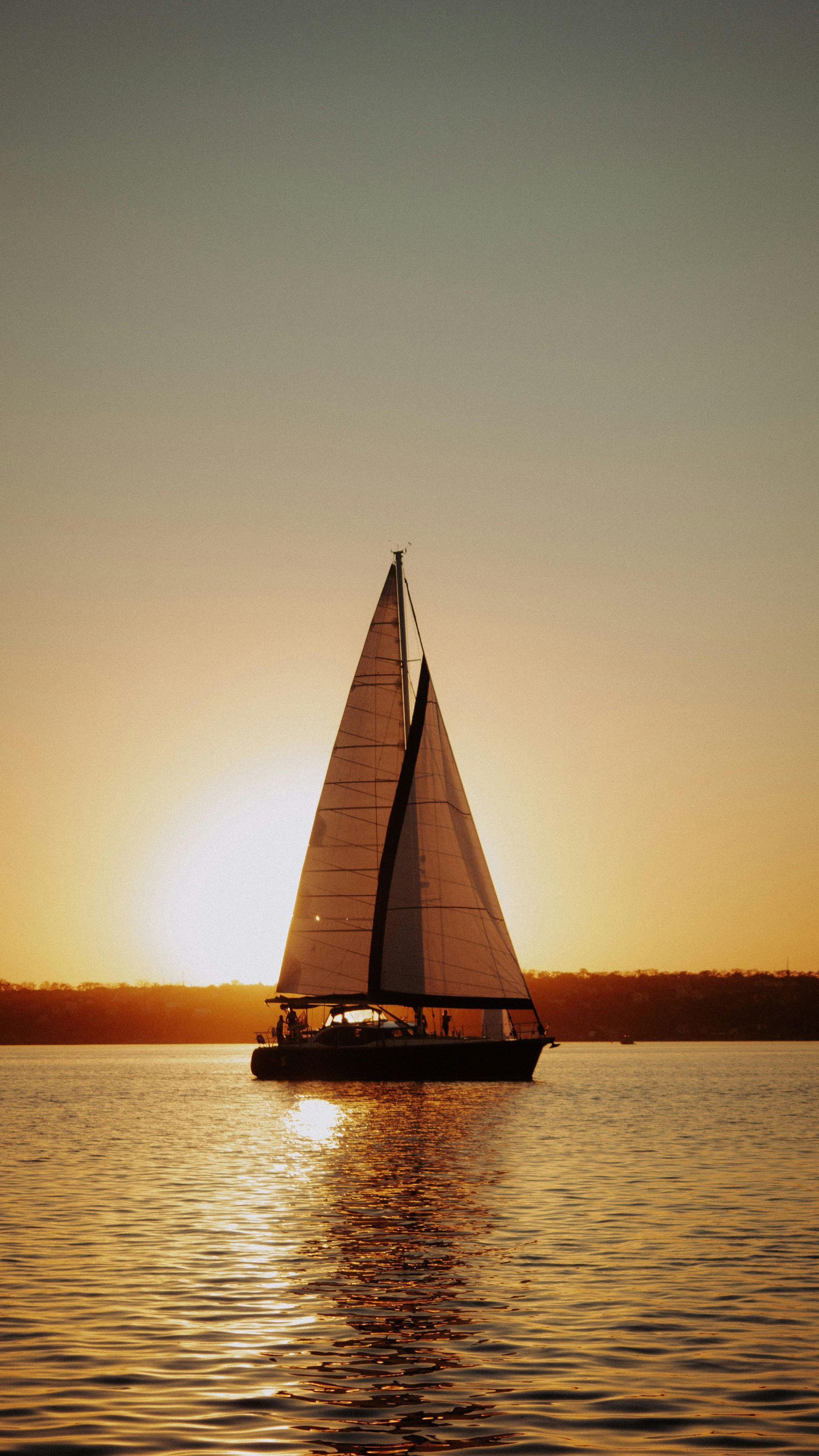 Sailboat on water at sunset; golden sunlight reflecting on the water and a clear sky.