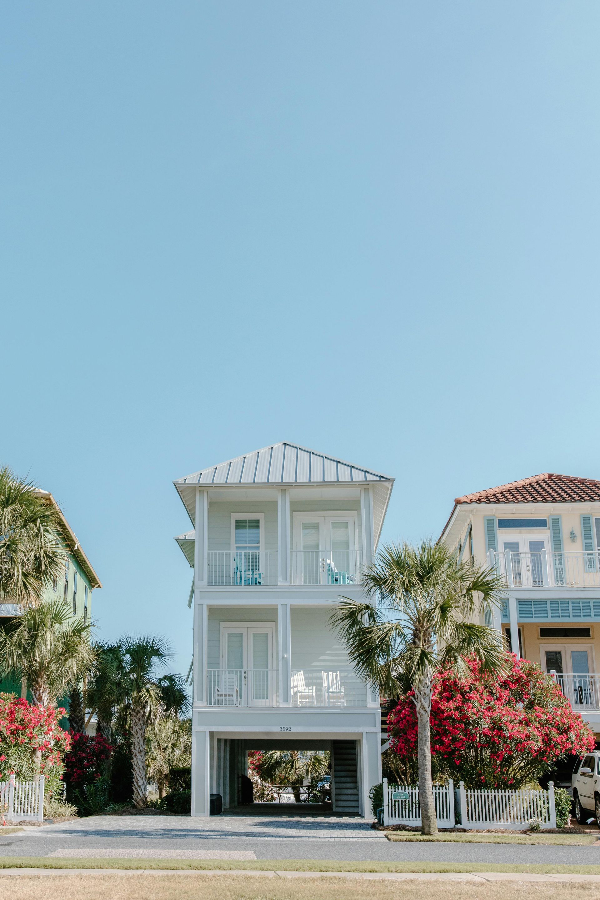 Three-story light blue beach house with balconies, white trim, set against a clear blue sky.