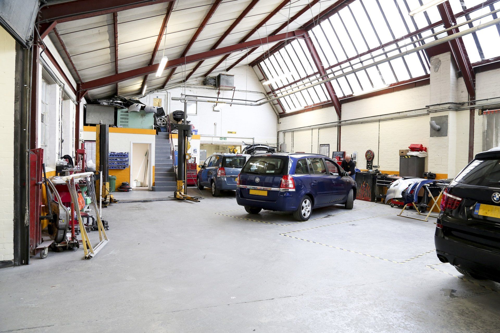 A blue car is parked in a garage next to a black car.