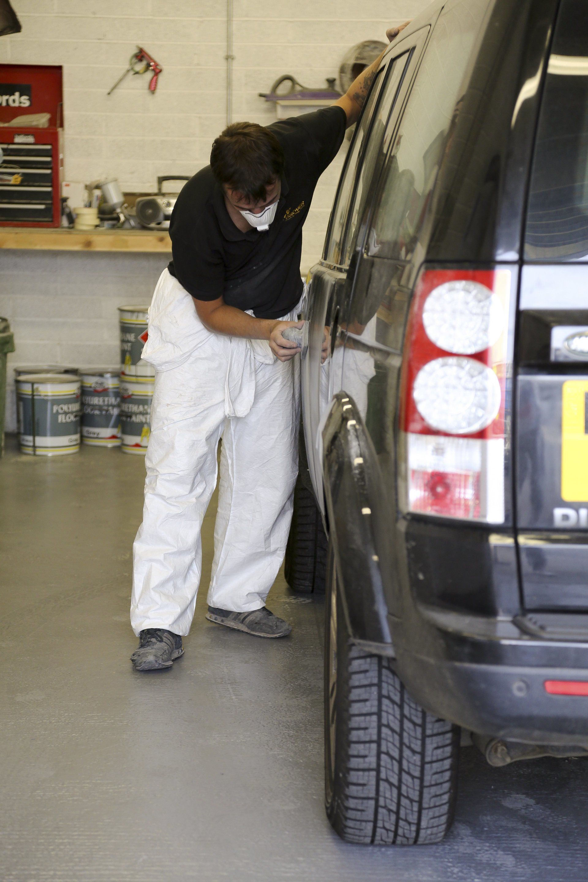 A man wearing a mask is working on a car in a garage.