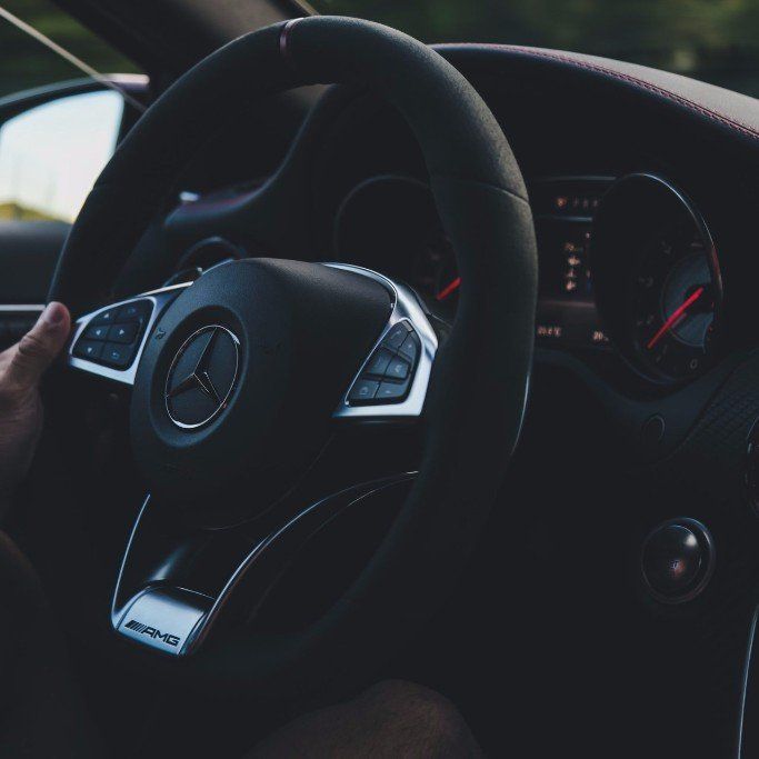 A person is driving a car with a mercedes logo on the steering wheel