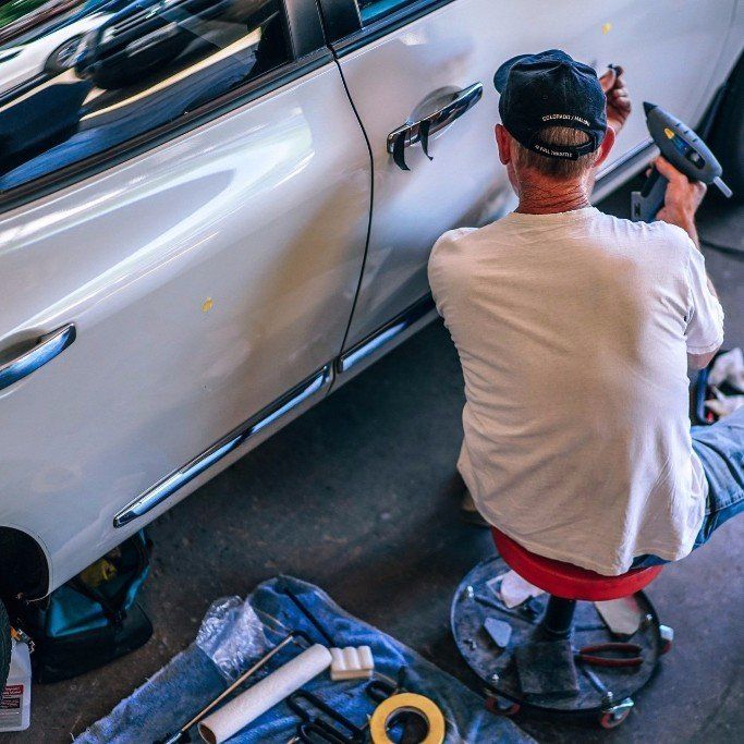 A man is sitting on a stool working on a car