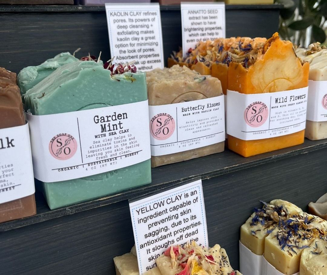 A display of colorful, handmade soaps with labels describing their ingredients and scents.