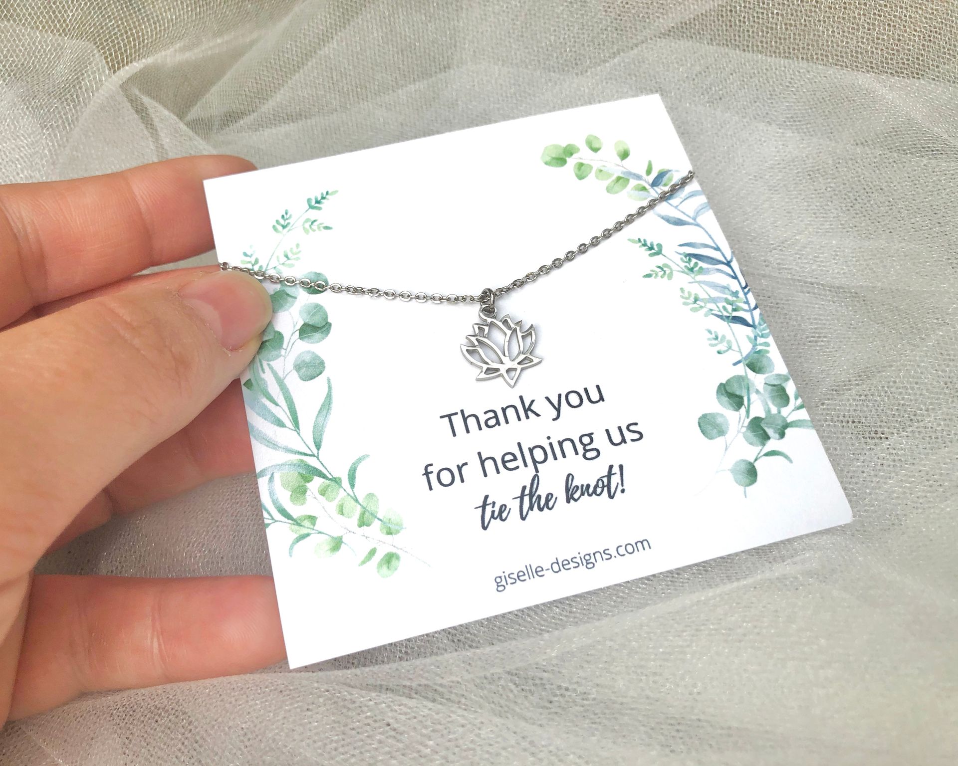 Hand holding a card with a silver lotus flower necklace. Card reads 