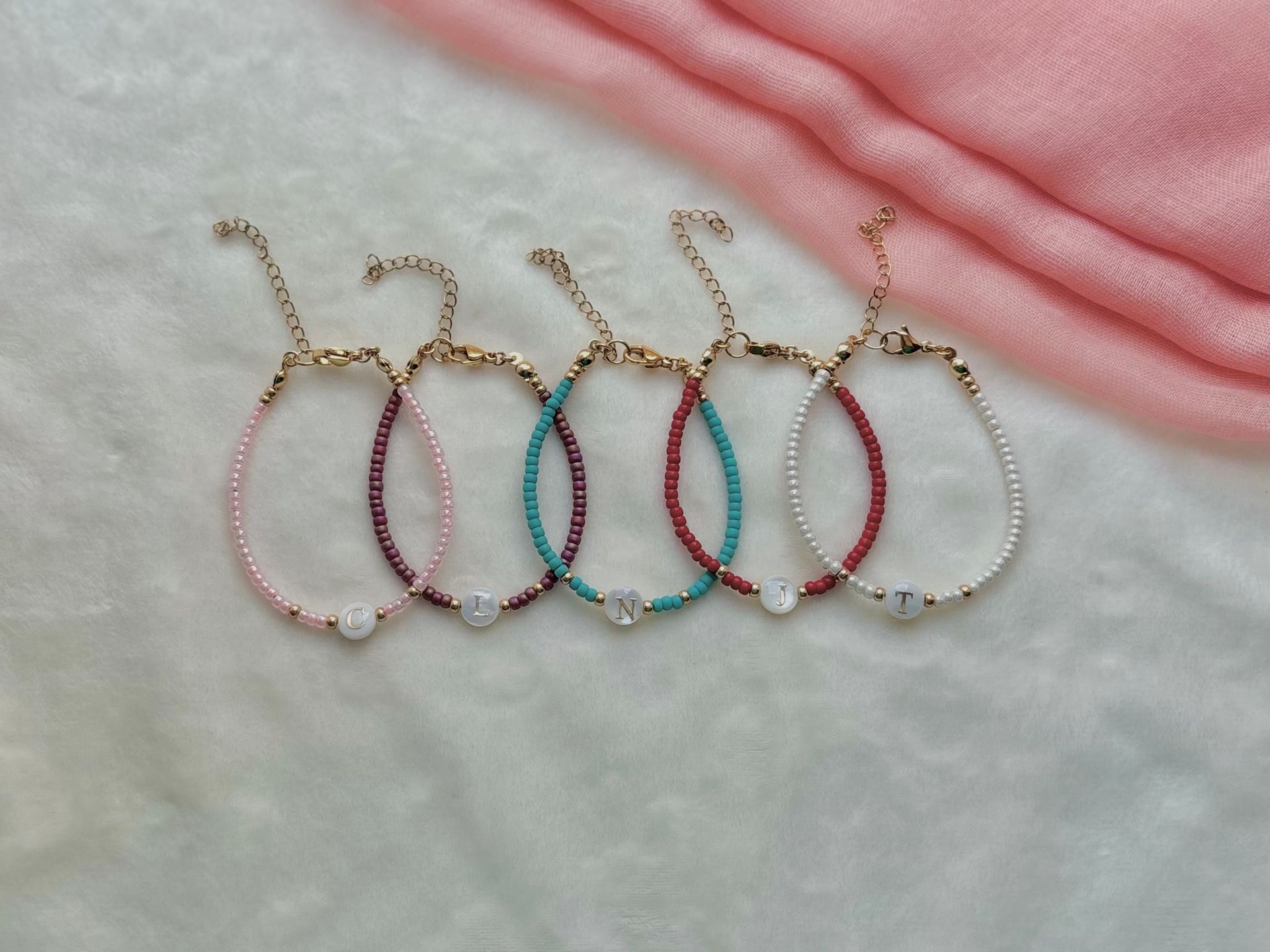 Person holding five beaded bracelets with letter charms.