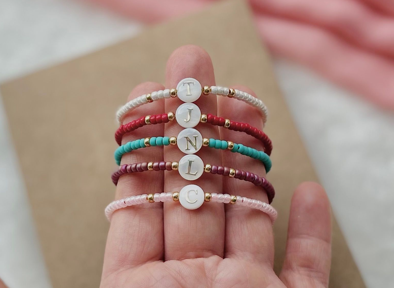 Hand holding five beaded bracelets spelling 