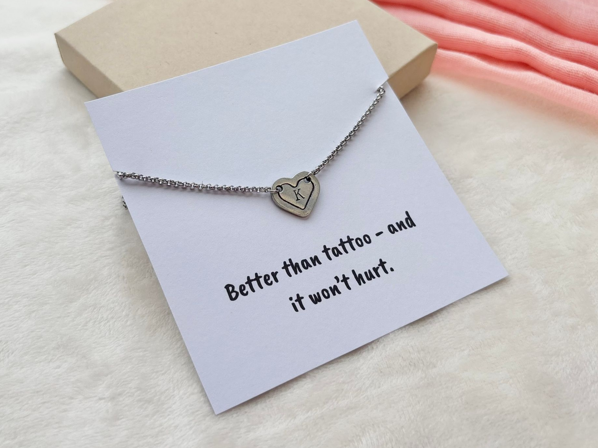 Silver necklace with a heart-shaped pendant, set against a pink cloth background.