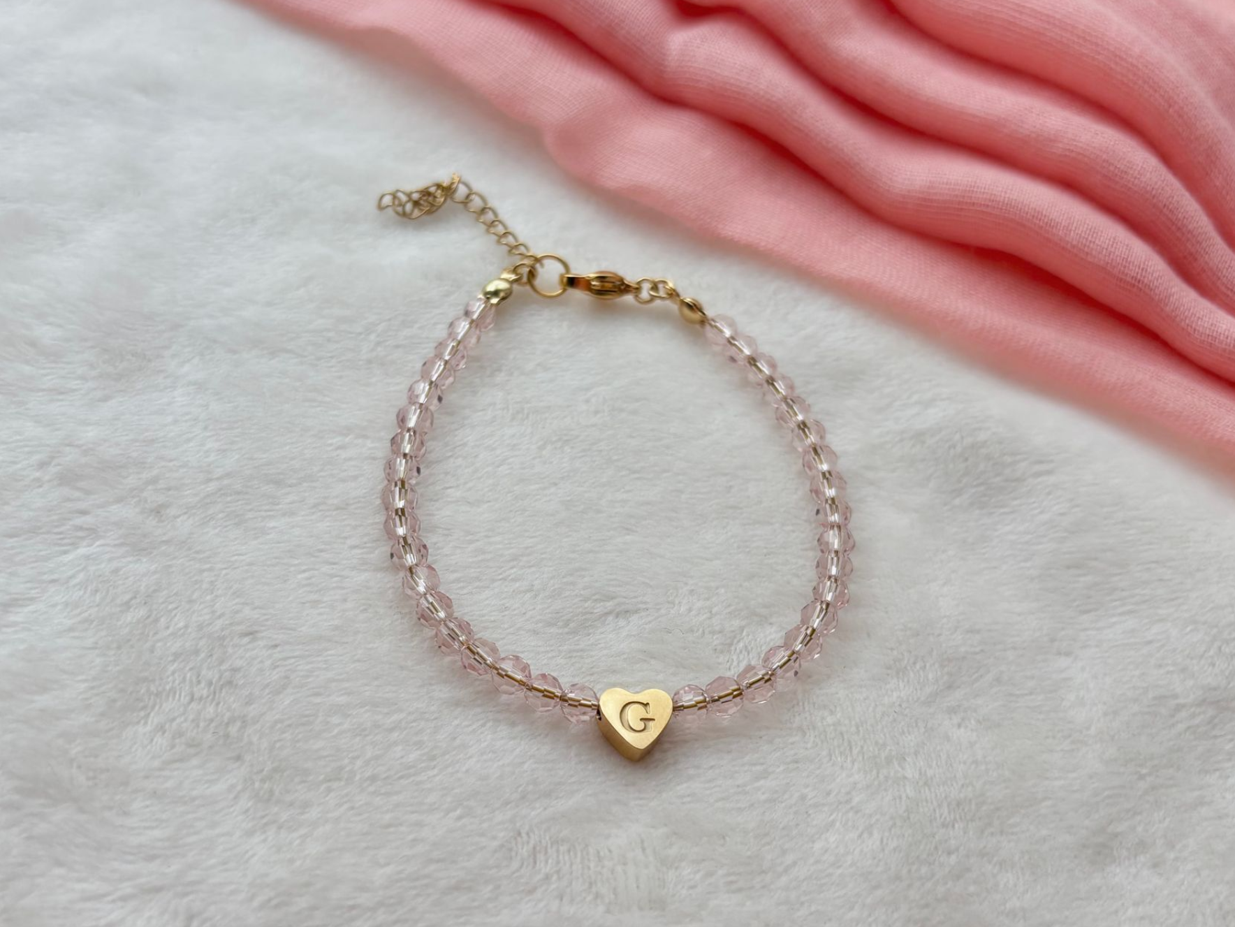 Pink beaded bracelet with a gold heart charm and the letter 