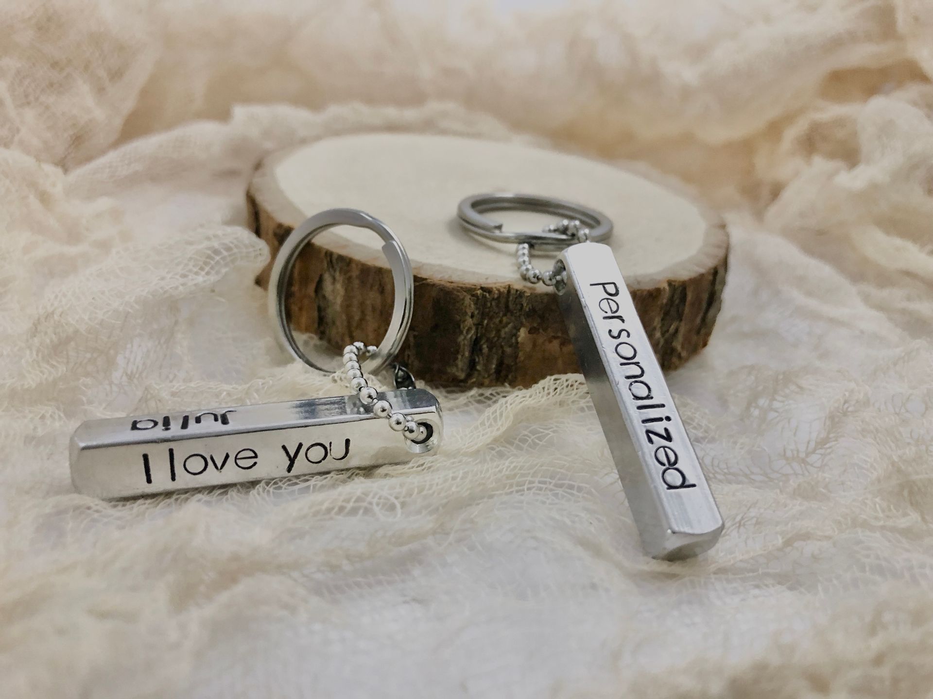Two silver, personalized keychains on a wood slice. One has a date, the other 