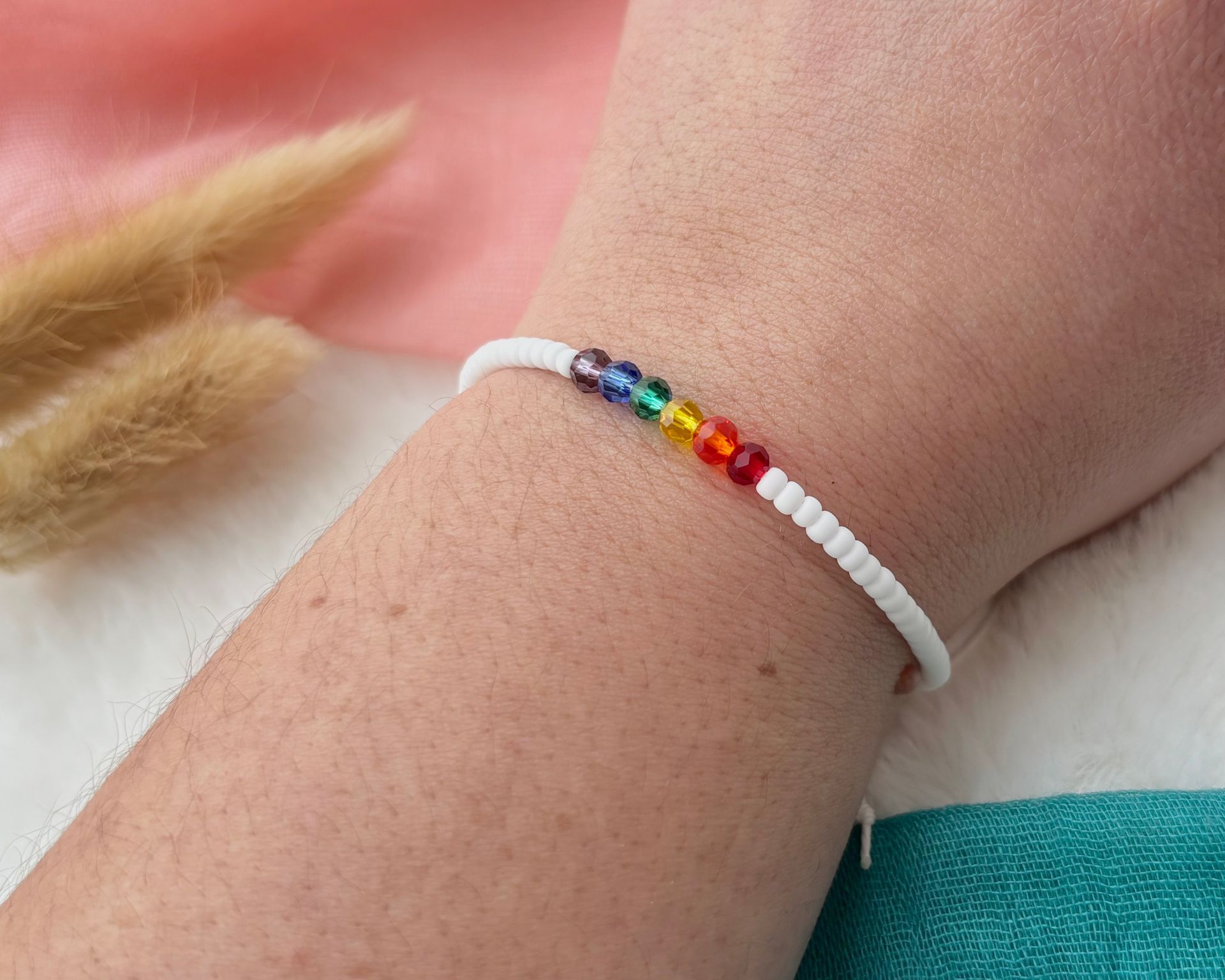 A bracelet with small rainbow-colored beads on a white card that reads, 