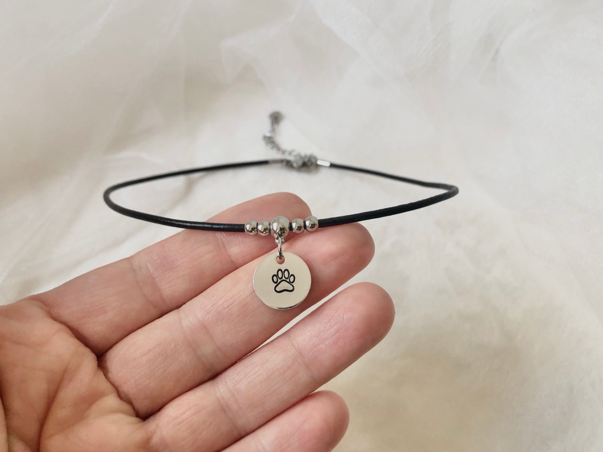 A hand holding a silver bracelet with a round charm displaying a zodiac symbol.