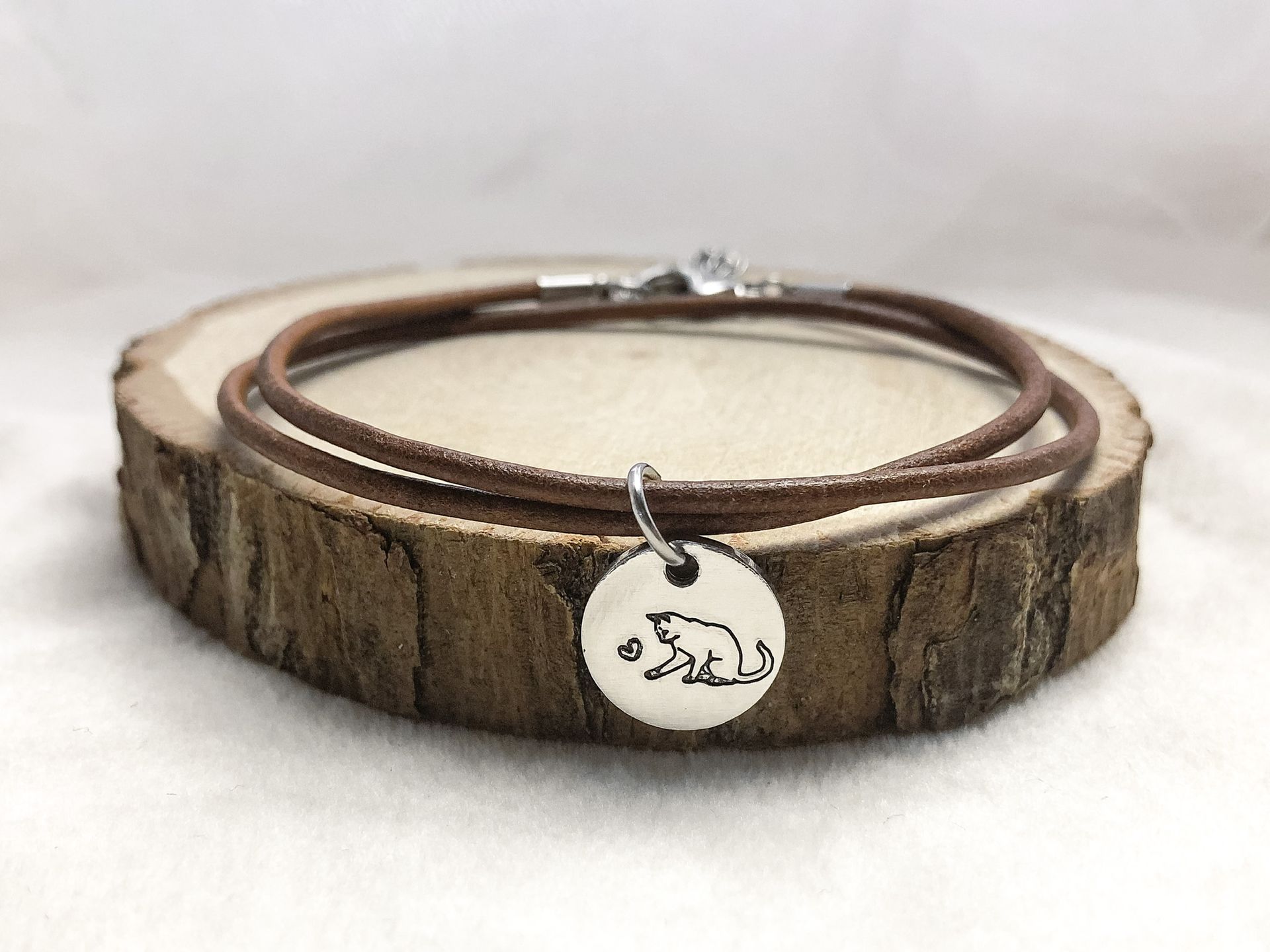 Brown leather bracelet with a cat pendant on a wooden surface.