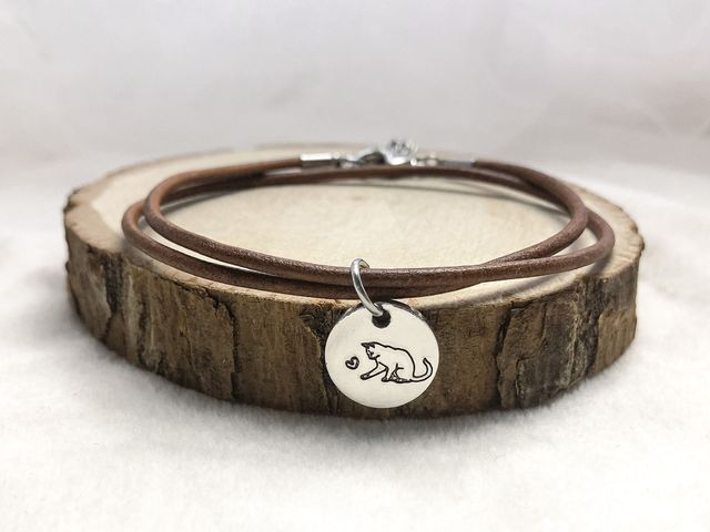 Brown leather bracelet with a cat pendant on a wooden surface.