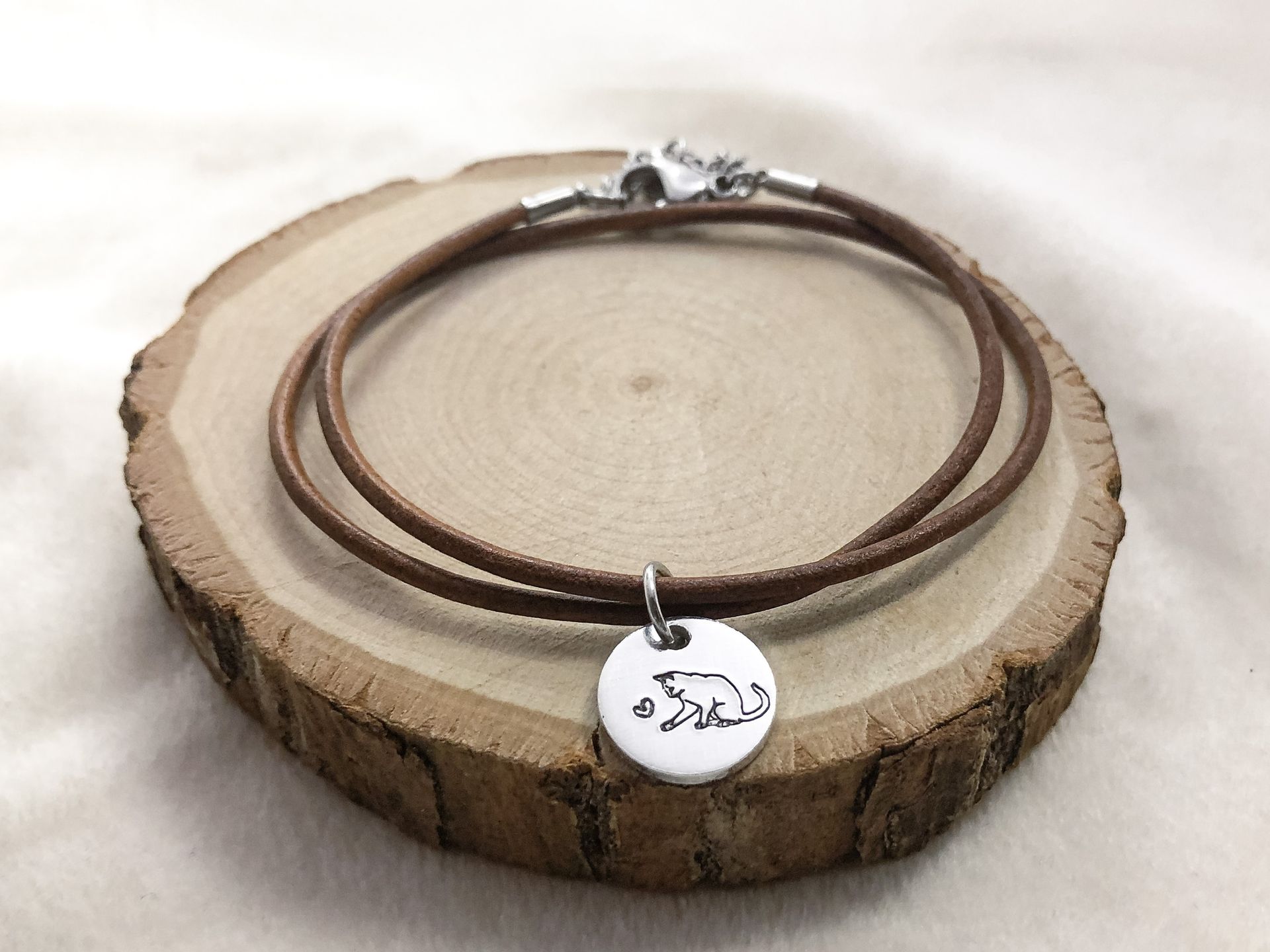 Brown leather bracelet with a cat pendant on a wooden surface.