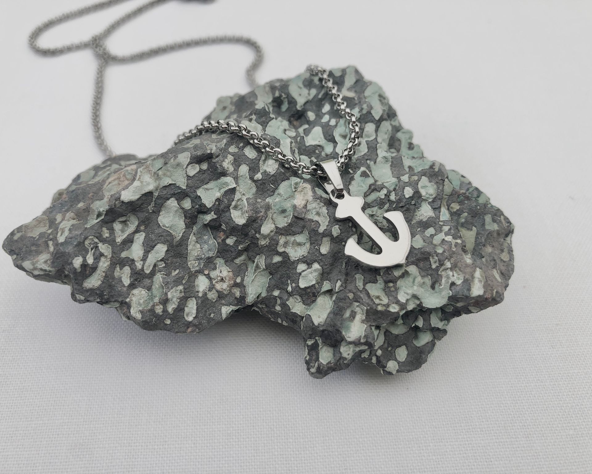 Silver anchor pendant on a textured rock, with a silver chain, against a white backdrop.