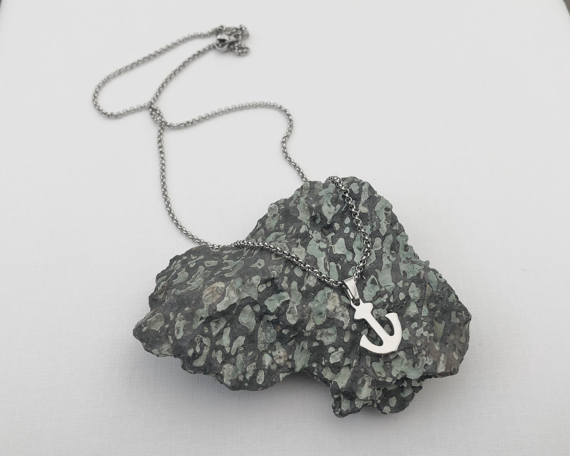 Silver anchor pendant on a textured rock, with a silver chain, against a white backdrop.