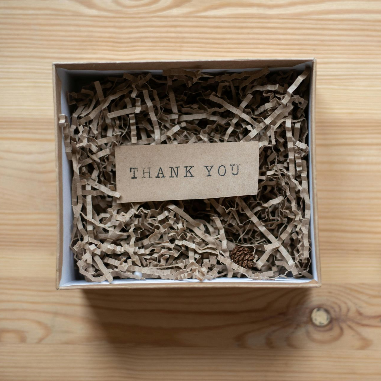 Open cardboard box filled with brown shredded paper and a small 