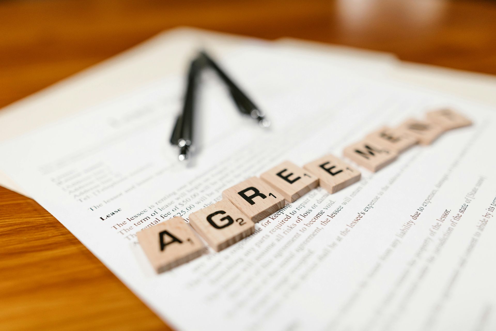 Agreement spelled out in Scrabble tiles on a document, with a pen.