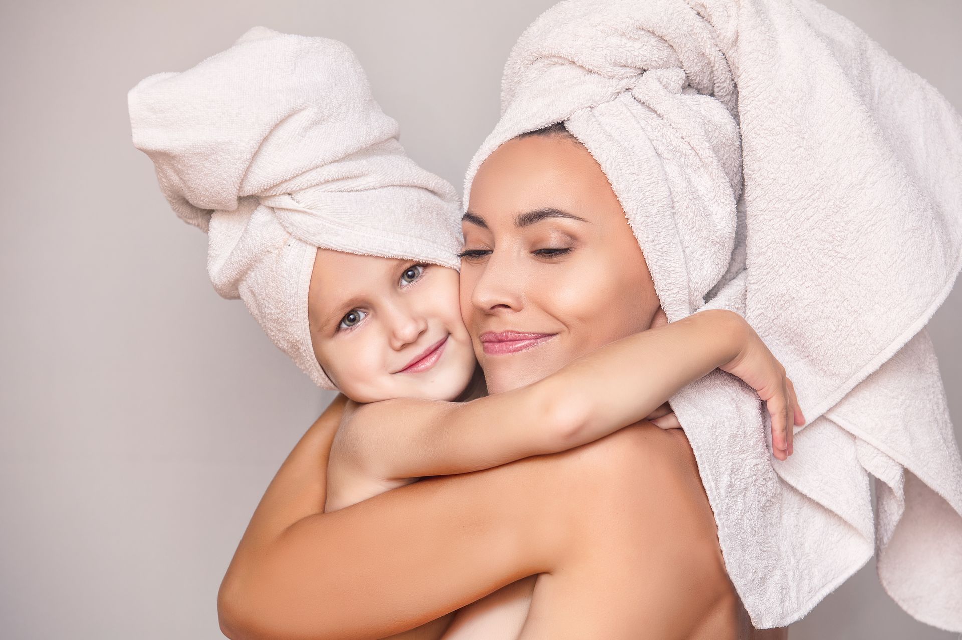 A woman and a child with towels wrapped around their heads are hugging each other.