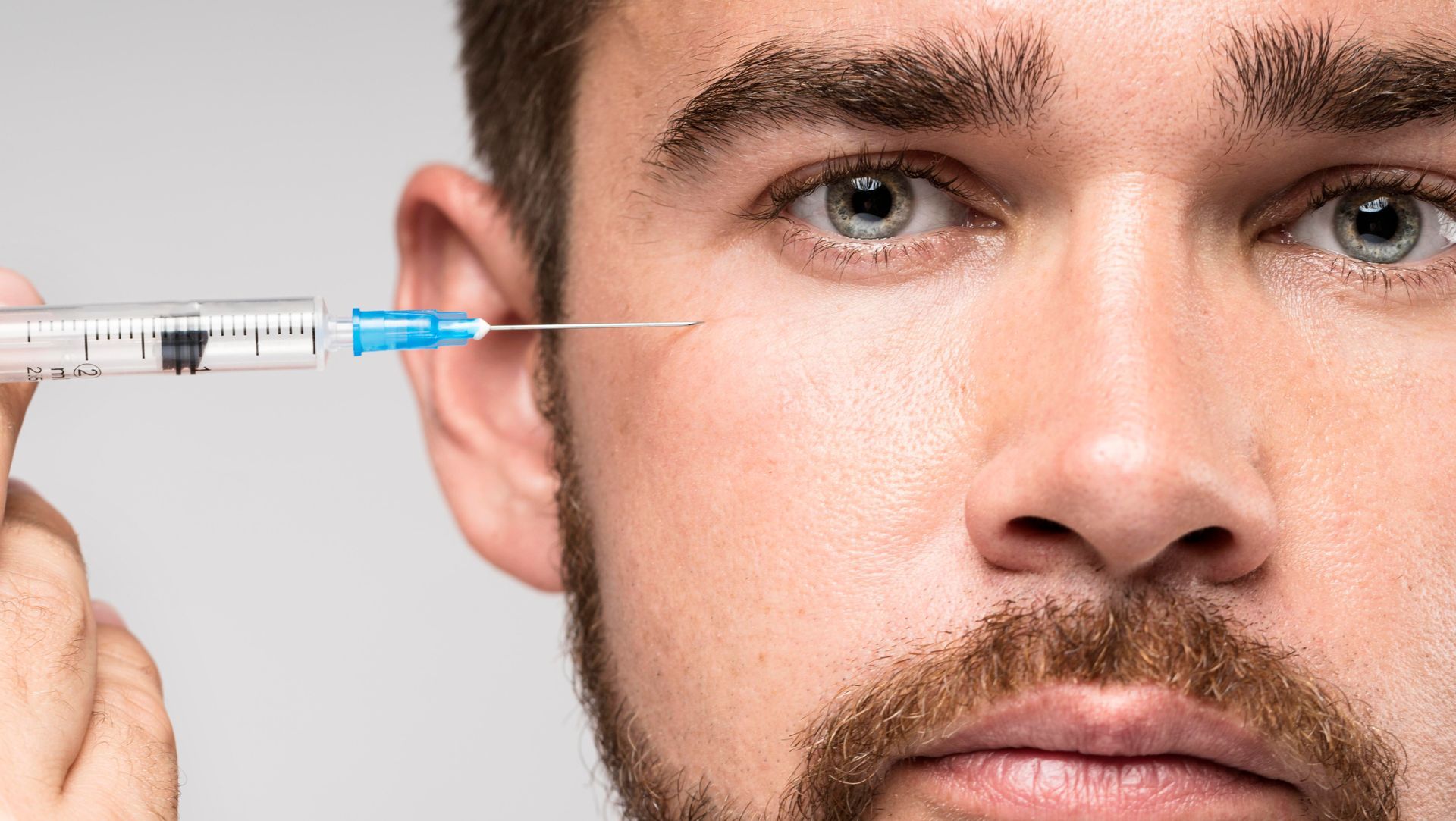 A man with a beard is holding a syringe in front of his face.