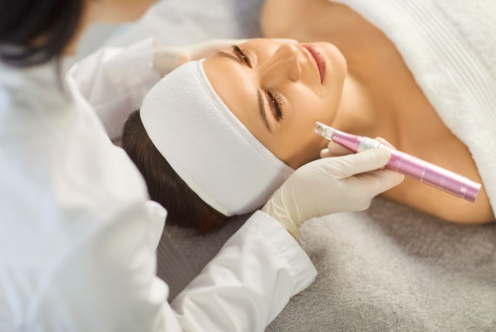A practitioner in gloves uses a handheld cosmetic pen on a person's face during a skin treatment procedure.