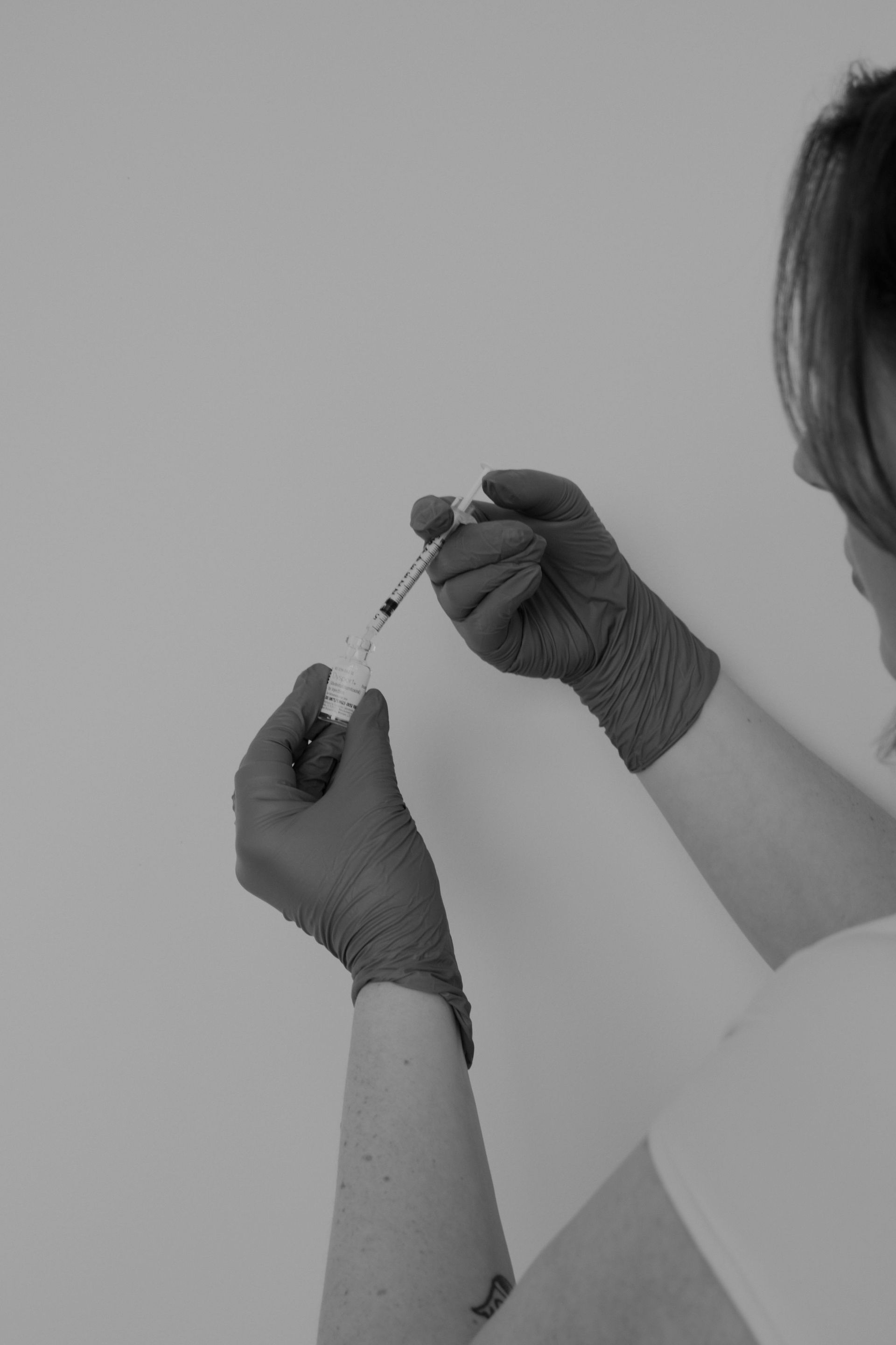 Person in gloves filling a syringe from a vial, likely administering a vaccine.