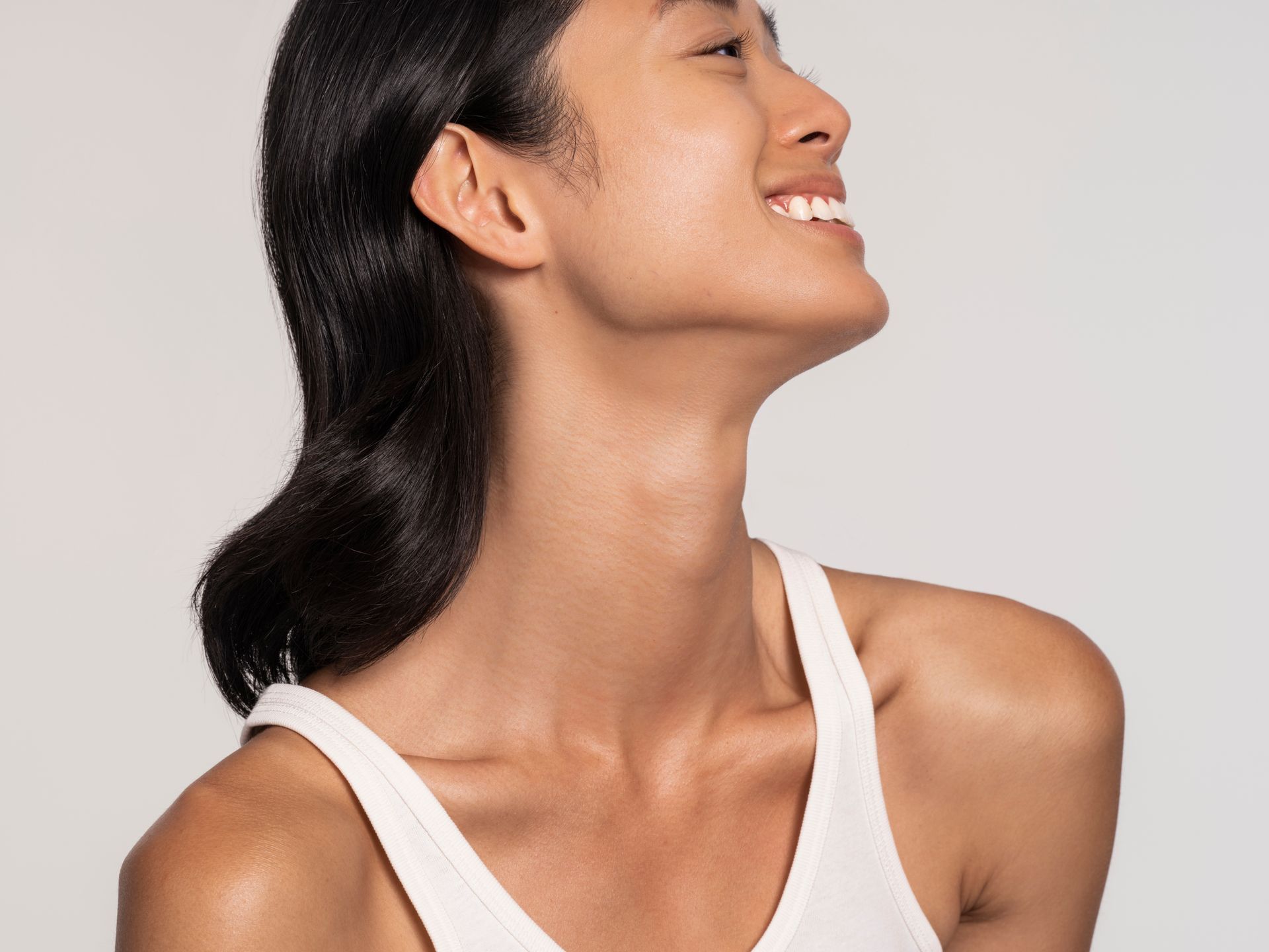 A woman in a white tank top is smiling and looking up.
