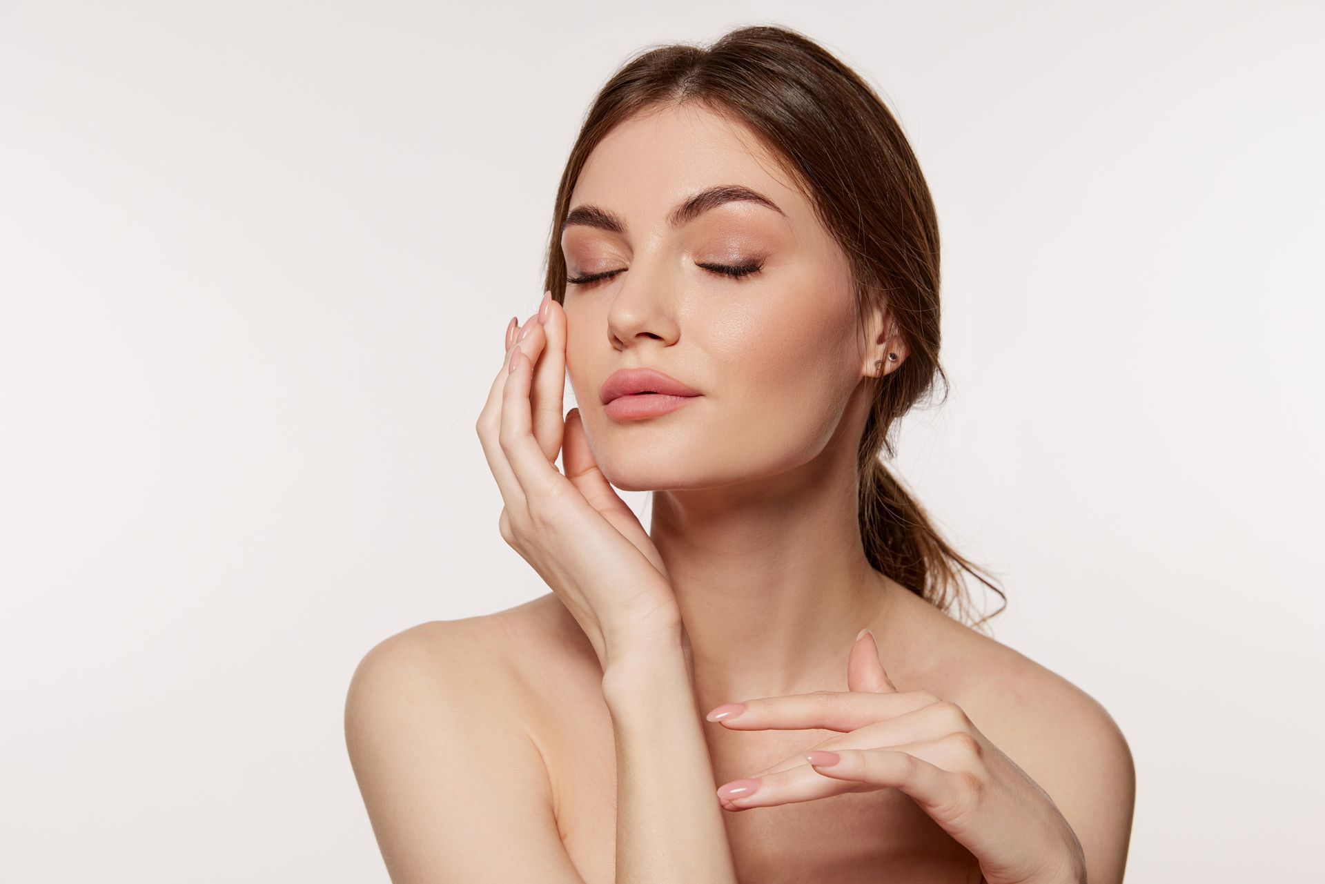 Woman with closed eyes gently touching her face, nude shoulders, soft lighting.