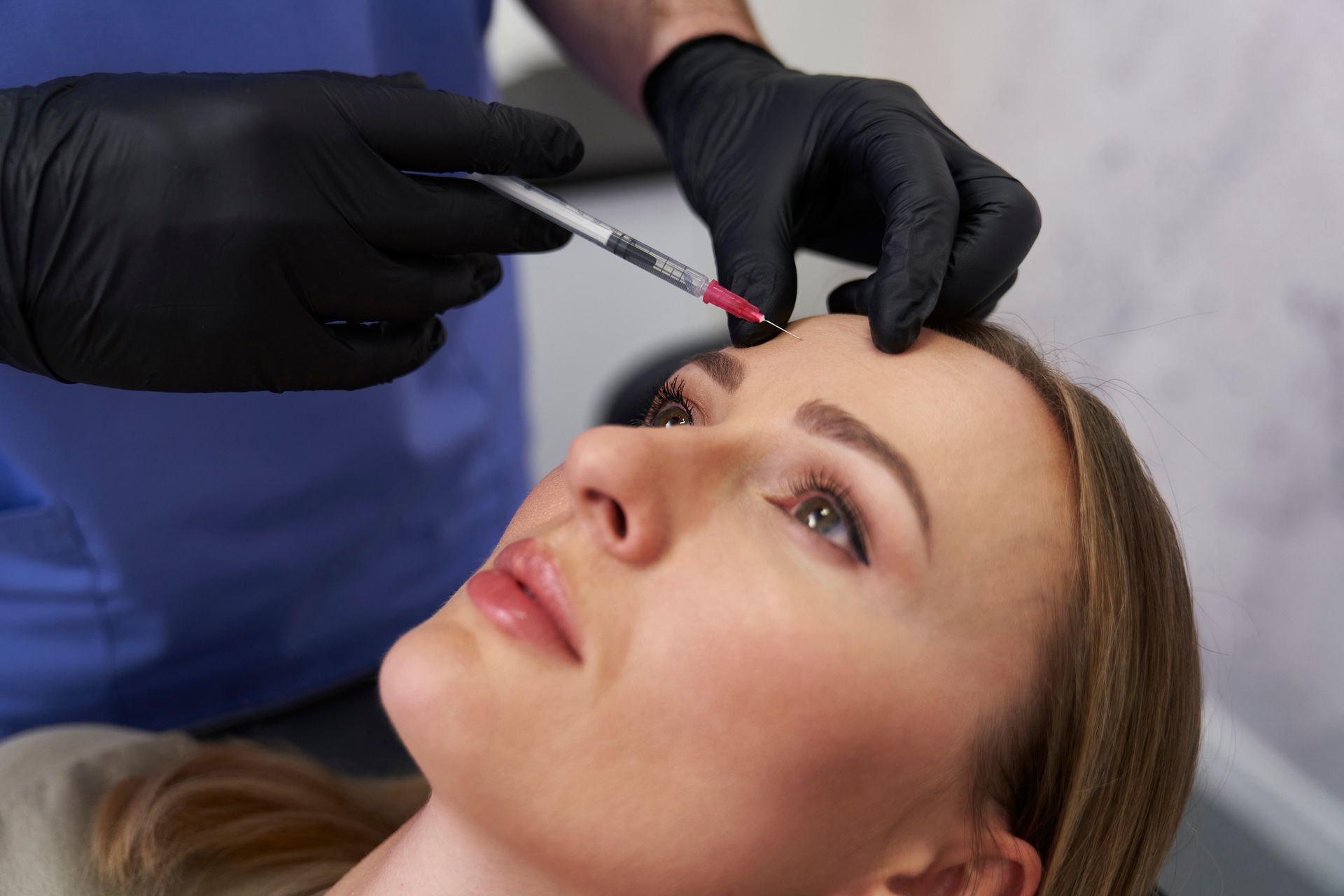 A person receiving an injection in the forehead; gloved hands, syringe.