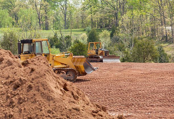 Two bulldozers are working on a dirt field.