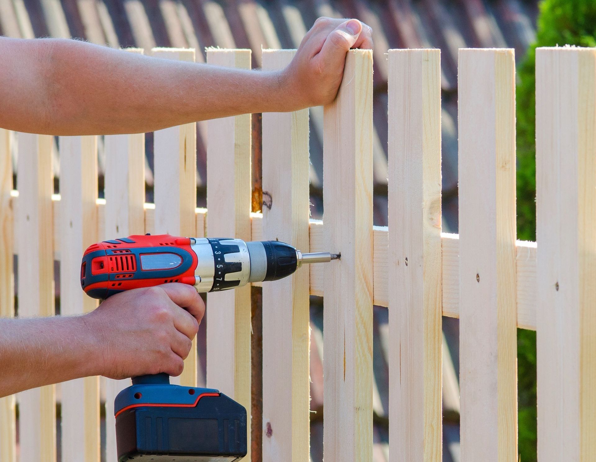 A man is using a drill to install a wooden fence.