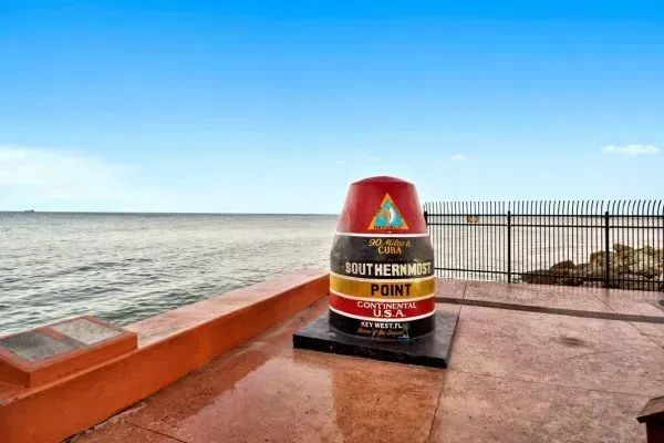 The Southernmost Point Buoy landmark in Key West, Florida, stands on a concrete pier overlooking the ocean.