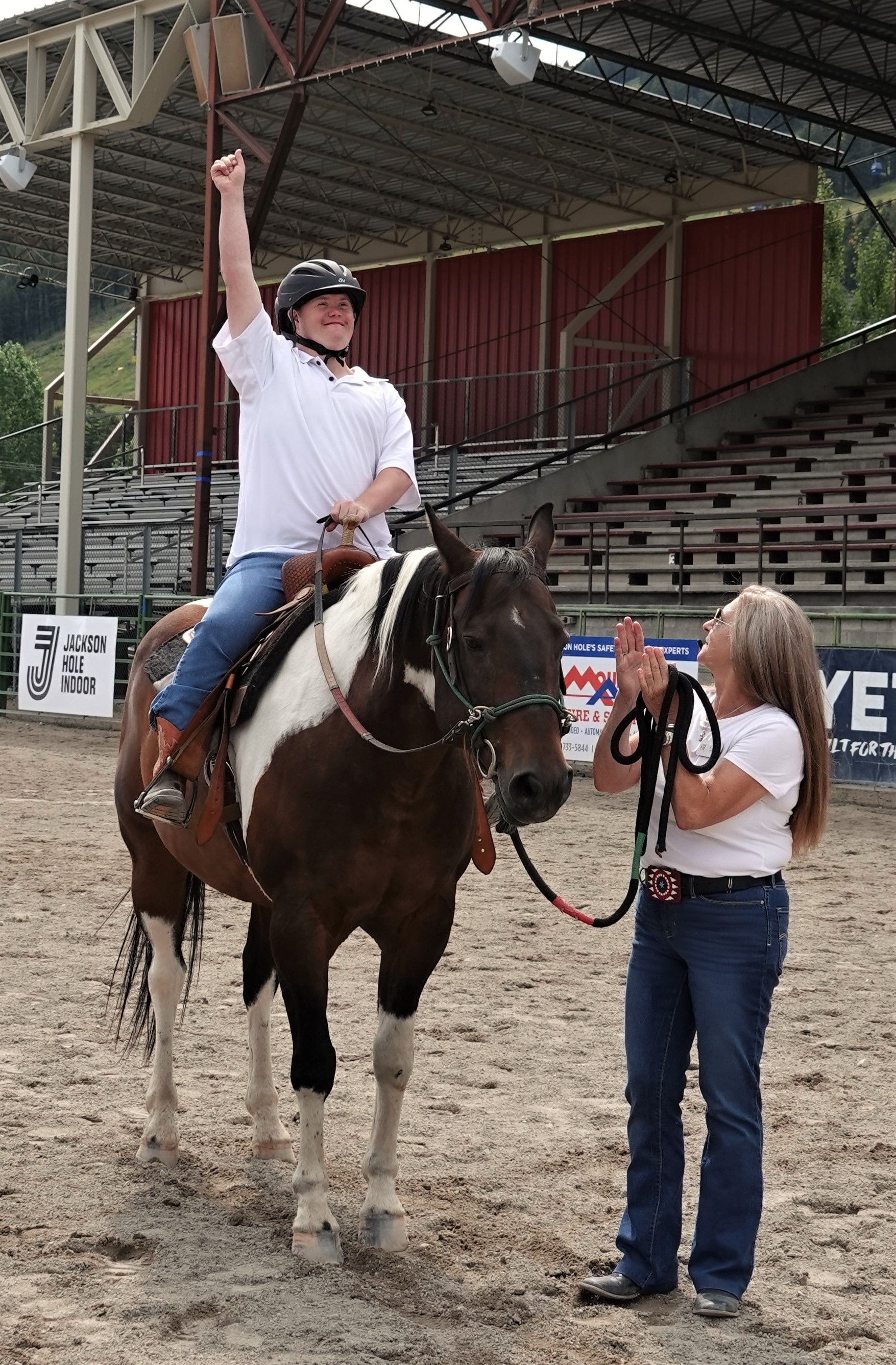 Teenager in cowboy hat leads a brown horse and a black foal in a grassy field.