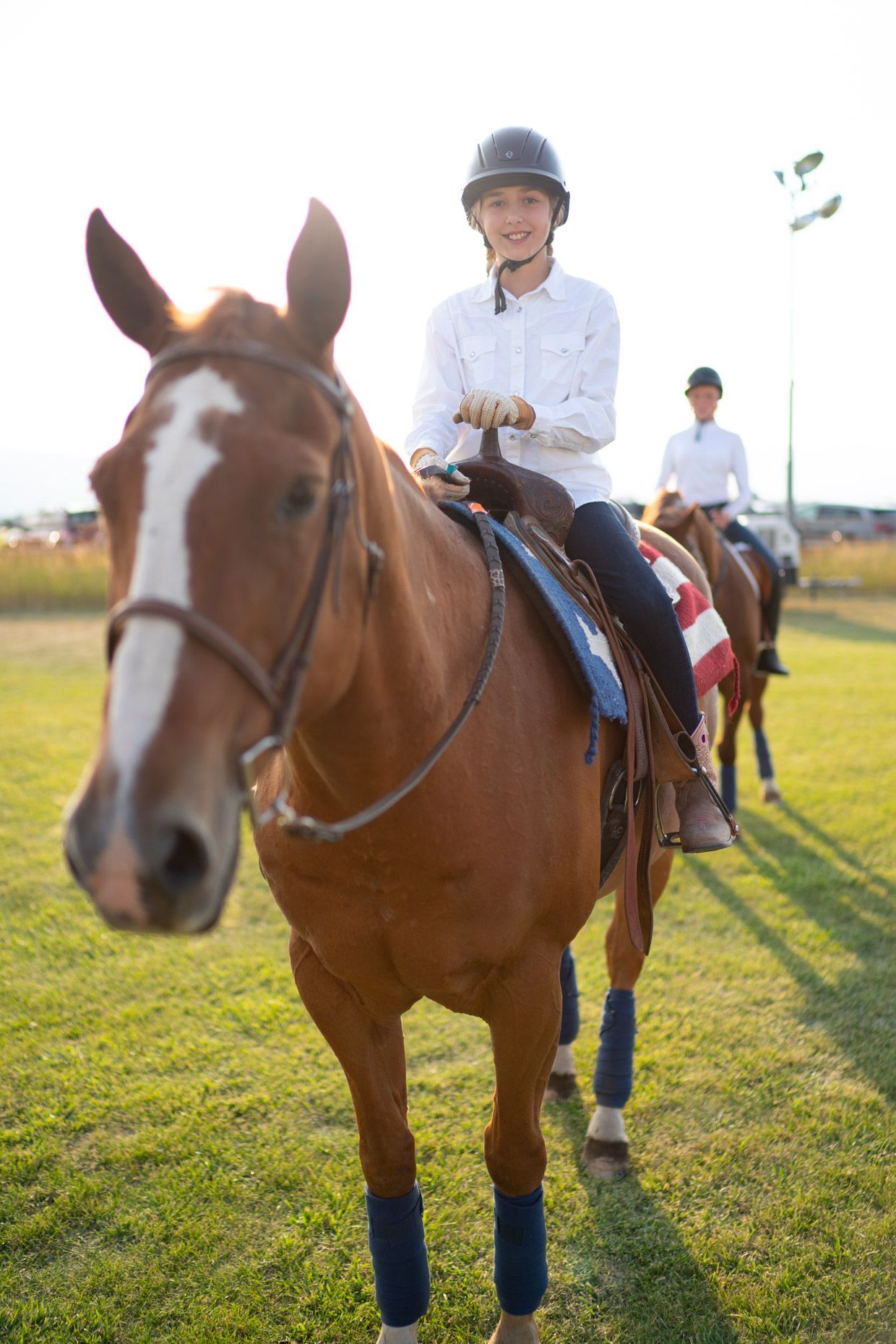 Woman riding a black horse in a field, wearing tan pants, black boots, and a green jacket.