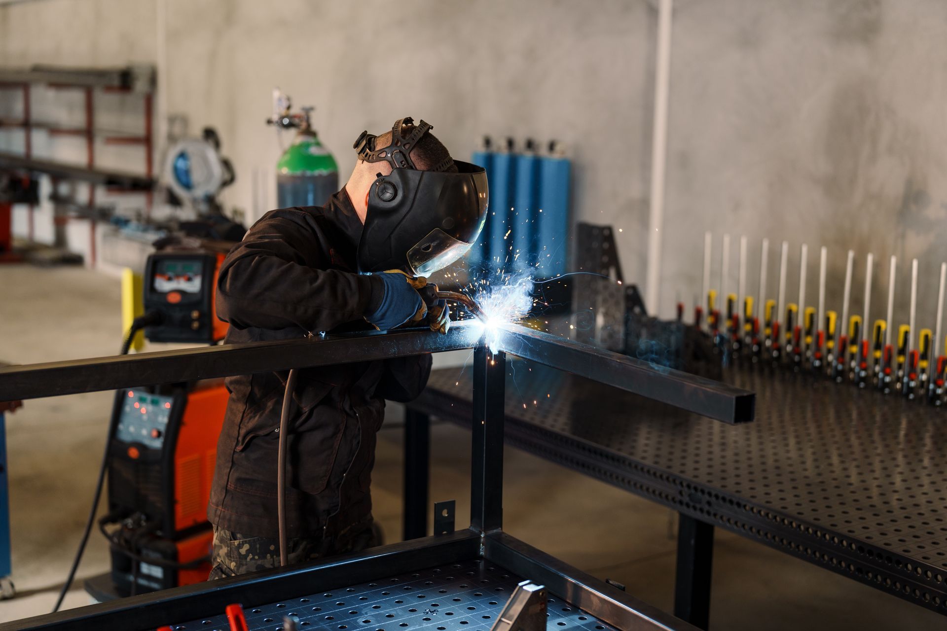 Welder in a workshop wearing a mask, welding metal frame; sparks fly. Welder in a workshop wearing a mask, welding metal frame; sparks fly.