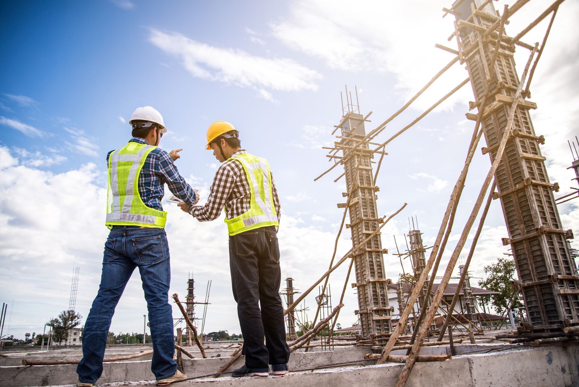 Two construction workers wearing safety vests and hard hats, inspecting a concrete structure on a sunny day.